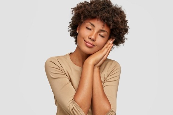 Woman standing up and closing her eyes while resting her head on her hands like a pillow