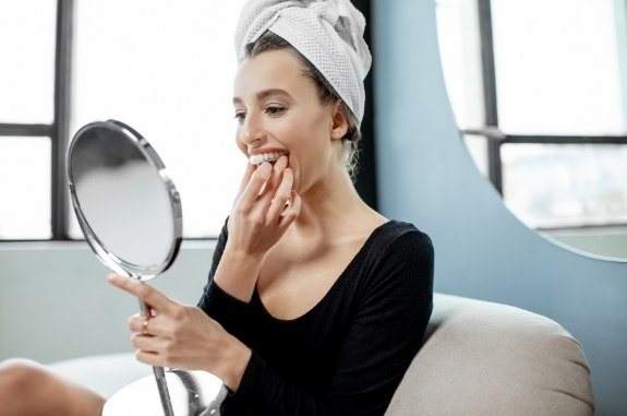 Woman with hair in towel placing at home teeth whitening tray in her mouth