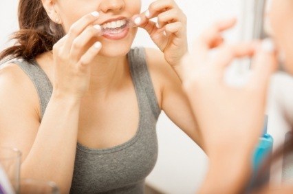 Woman placing teeth whitening strip over her upper teeth