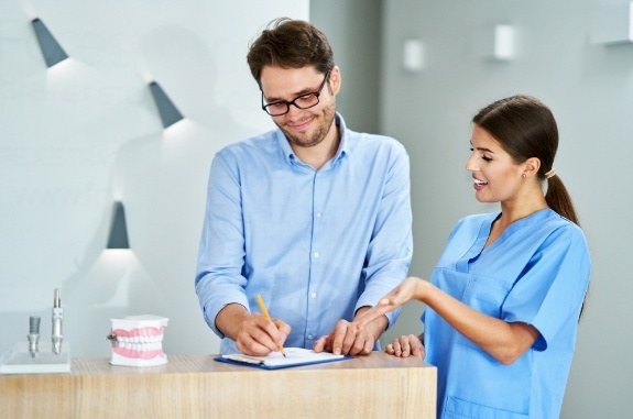 Man writing on clipboard with dental team member