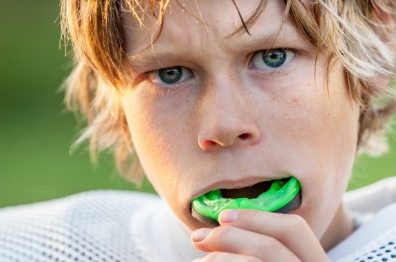 Boy placing light green athletic mouthguard into his mouth