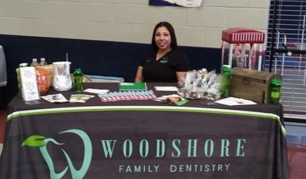 Dental team member sitting at table with Woodshore Family Dentistry table cover at Clute community event