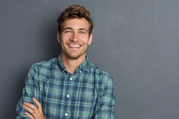 Smiling man in green and blue plaid shirt standing with arms crossed