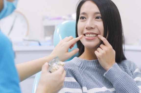 Woman in dental chair pointing to her smile