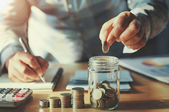 Man at desk dropping a coin in his coin jar