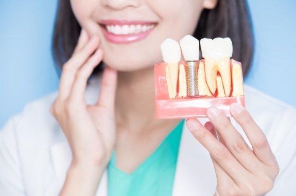 Dentist touching her jaw while holding a dental implant model