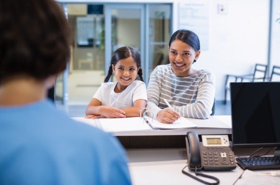 Woman with her child writing on paper at dental office front desk