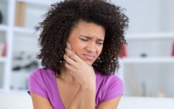 Woman in purple blouse holding her jaw in pain