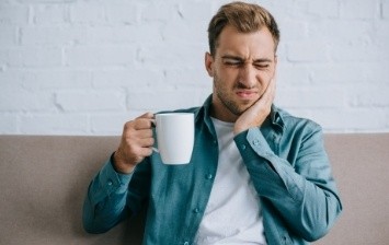 Man with white coffee mug holding his jaw in pain