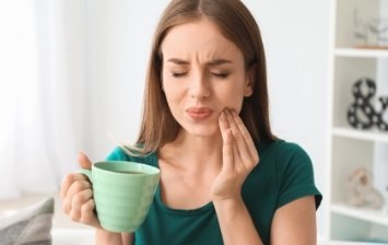 Woman with green coffee mug holding her jaw in pain