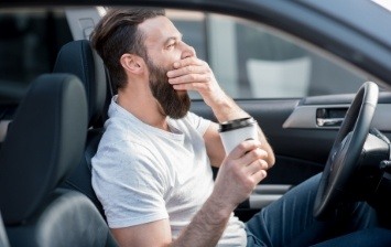 Man with coffee yawning while sitting in car