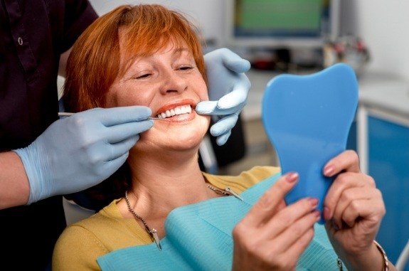 Redheaded woman seeing her smile in mirror after getting dentures