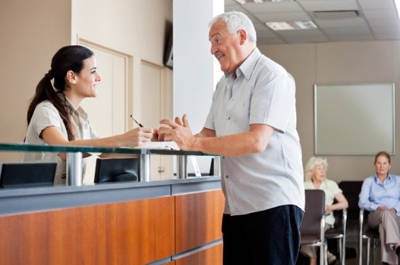 Senior man talking to dental team member at front desk