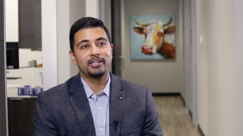 Doctor Pattni sitting in dental office hallway with painting of longhorn in background