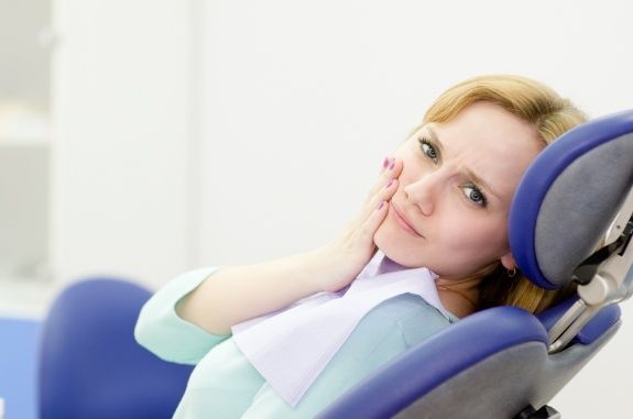 Woman in dental chair holding the side of her face in pain