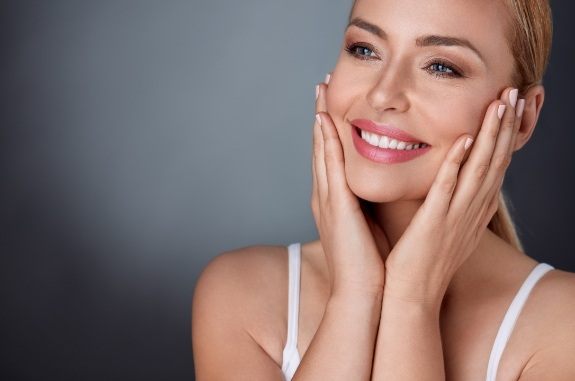 Woman in white tank top holding her cheeks and smiling