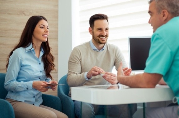 Two dental patients talking to dental team member at desk