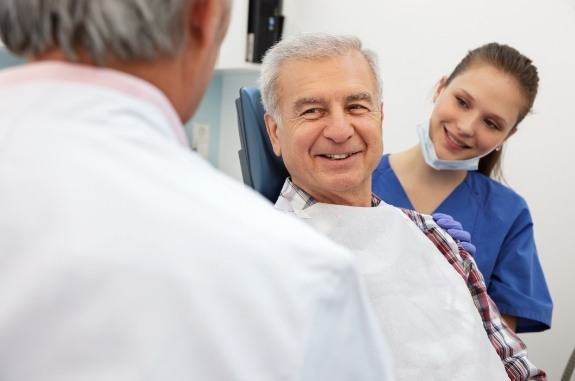 Smiling elderly man talking to dentist and dental team member