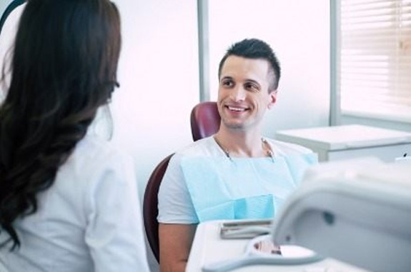Man in dental chair talking to dental team member