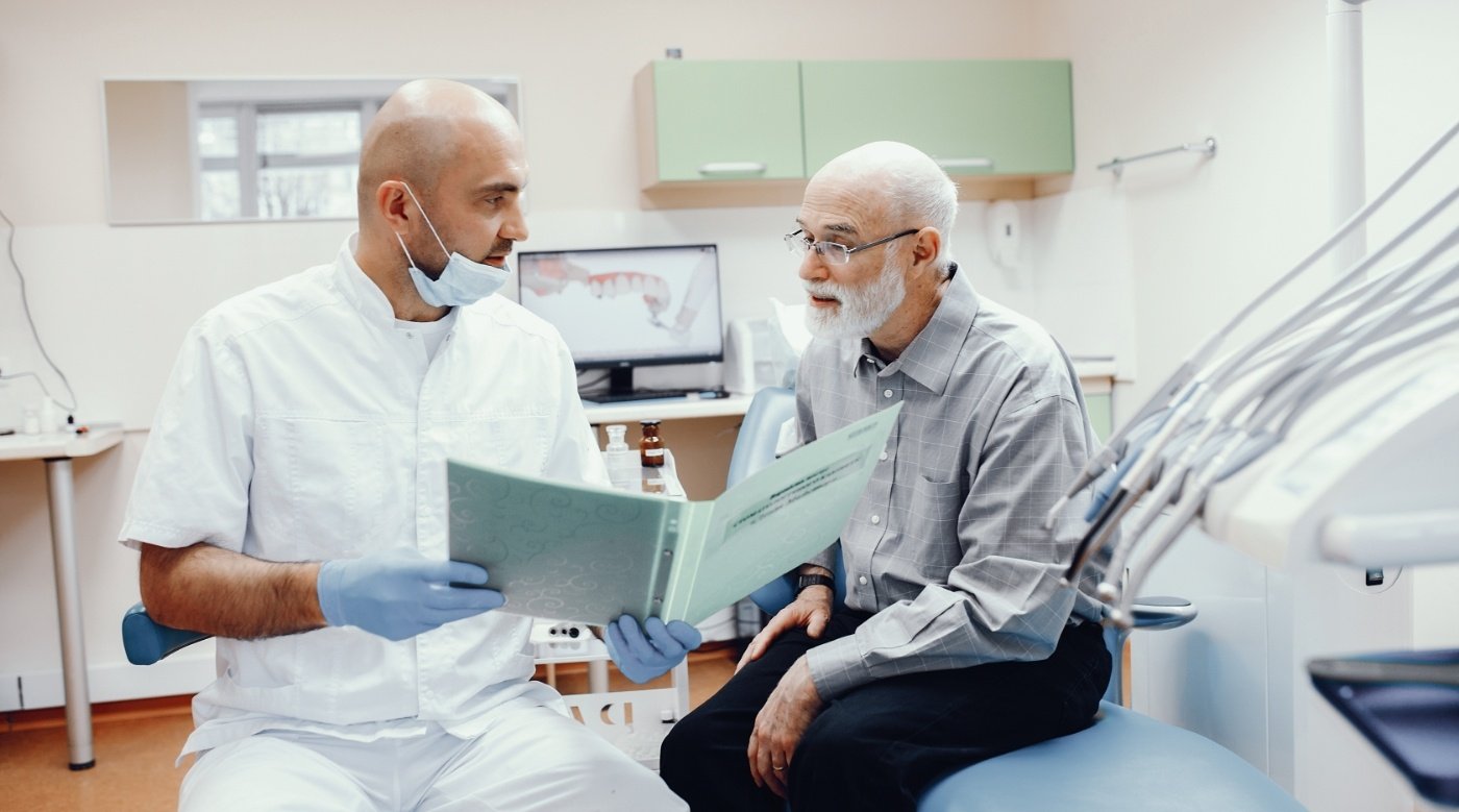 Dentist showing a binder to an elderly man in dental chair