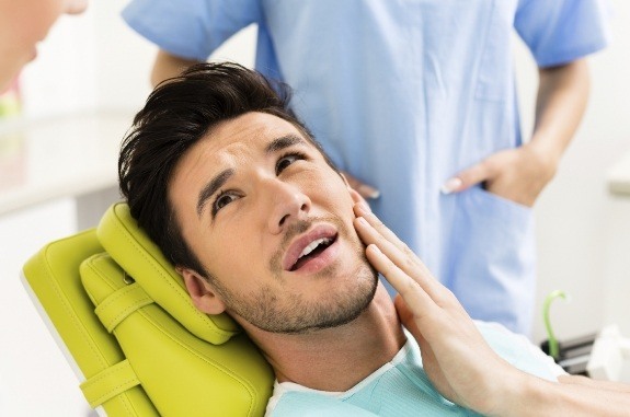 Man holding his jaw in pain while talking to dentist