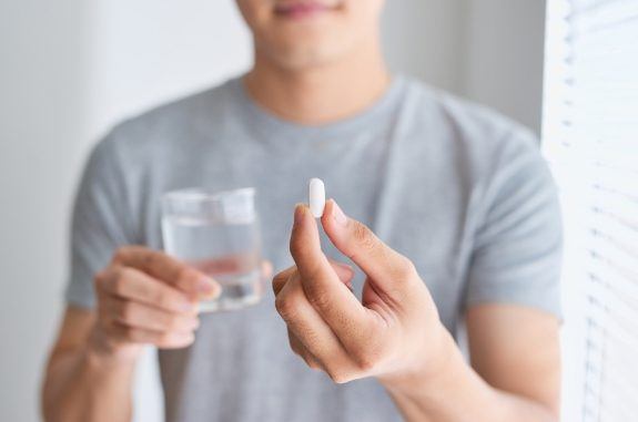 Man holding a pill in one hand and a glass of water in the other