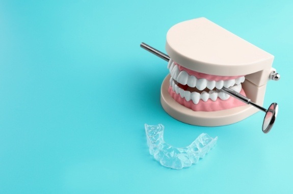 Model of teeth biting on dental mirror next to clear aligner