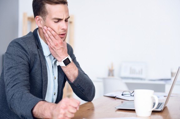 Businessman sitting at desk holding his jaw in pain