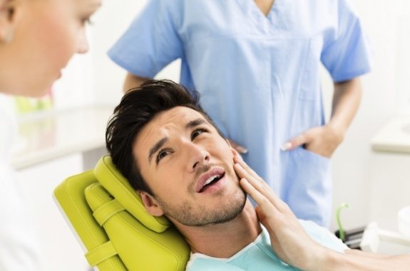 Man holding his jaw in pain while talking to his dentist
