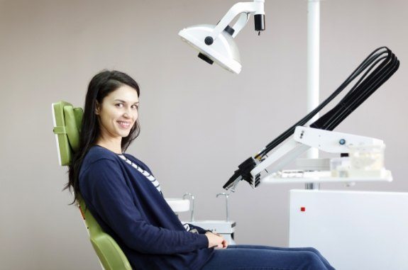 Smiling woman in dark blue blouse sitting in dental chair