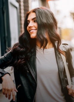 Woman in leather jacket leaning against brick wall