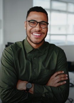 Man in dark green button up shirt smiling while standing with arms crossed