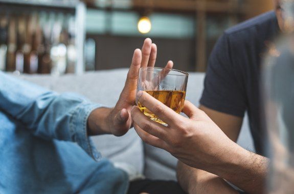 Person holding their hand palm outward to refuse a drink another person is offering