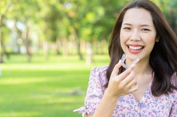 Smiling woman at a park holding an Invisalign clear aligner