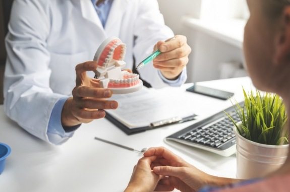 Dentist showing a model of teeth to a patient sitting across desk