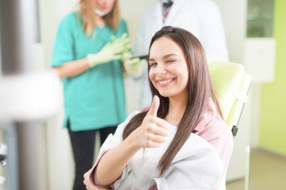 Smiling woman winking and giving thumbs up while sitting in dental chair