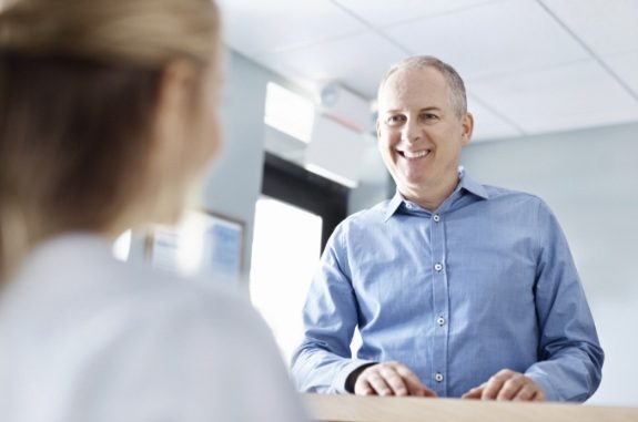 Man in denim shirt talking to dental team member at front desk