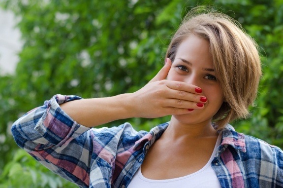 Young woman outdoors covering her mouth with her hand