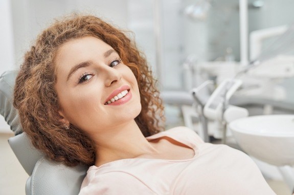 Woman in peach colored blouse smiling in dental chair