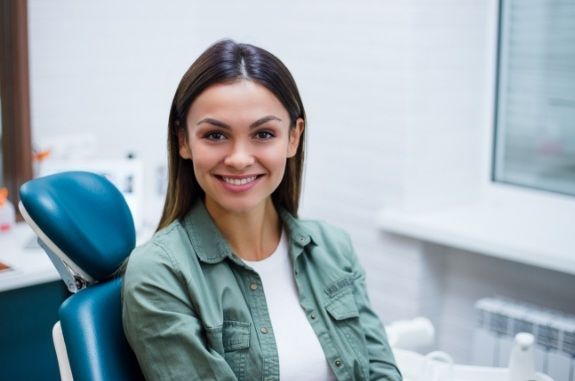 Woman in green shirt smiling in dental chair after getting veneers in Clute