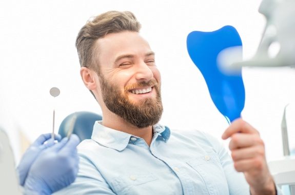 Bearded man seeing his new smile in mirror in dental chair