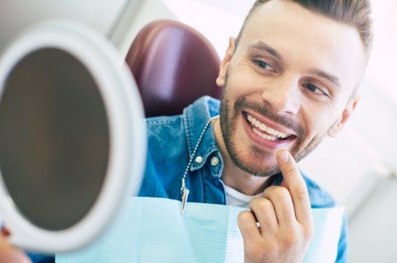 Dental patient looking in mirror and pointing to his smile