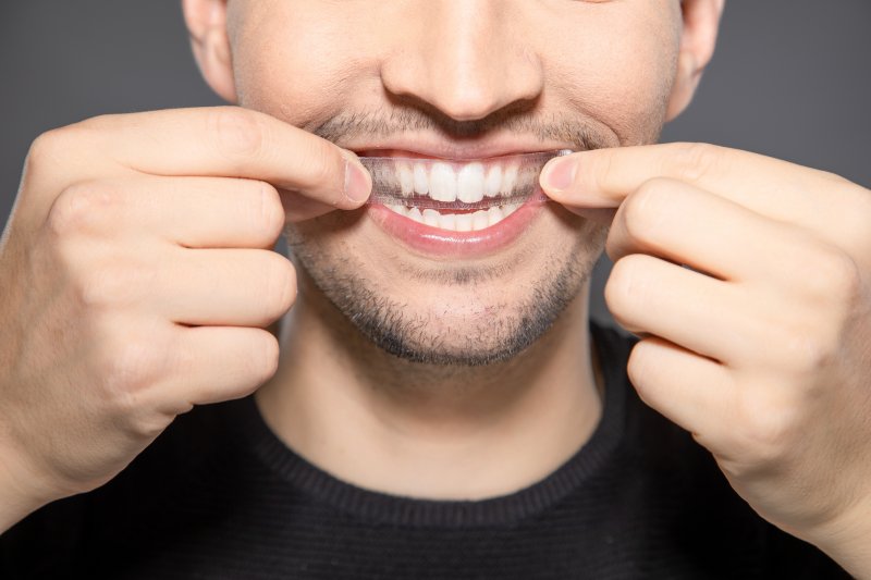 A smiling man trying to apply teeth whitening strips to his mouth.